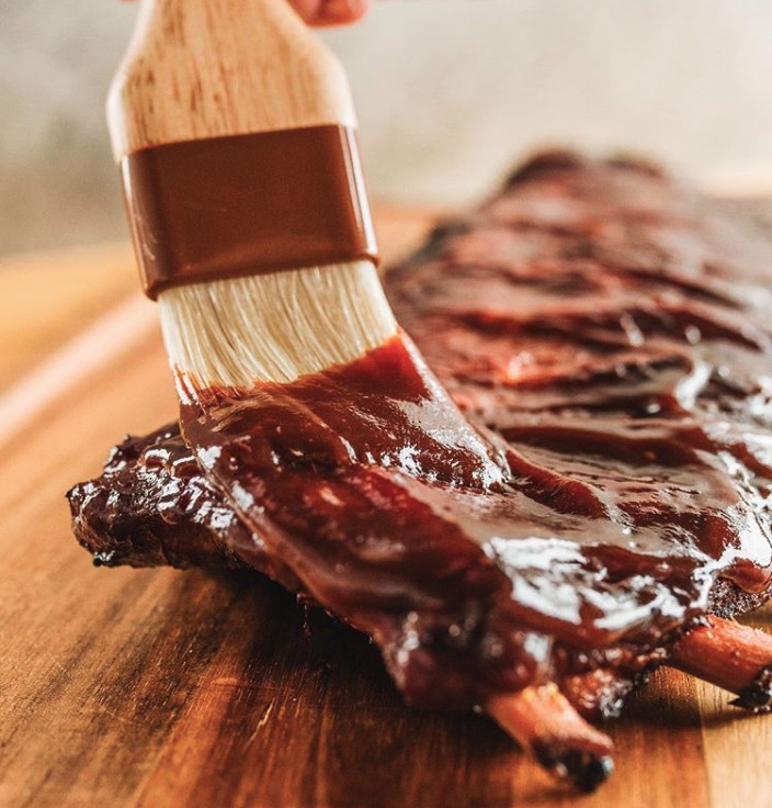 Ribs getting BBQ sauce slathered on with brush